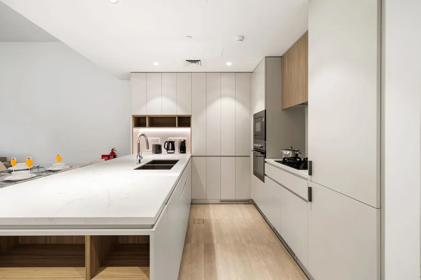 A modern kitchen with white cabinetry, a long island, and built-in appliances.