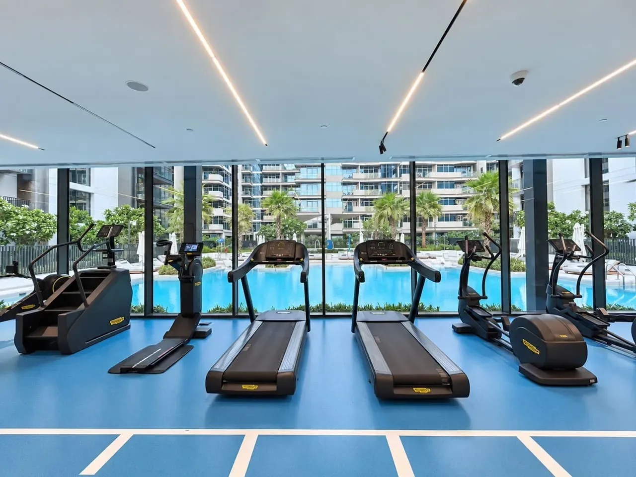 A fitness room with treadmills and exercise bikes beside floor-to-ceiling windows.
