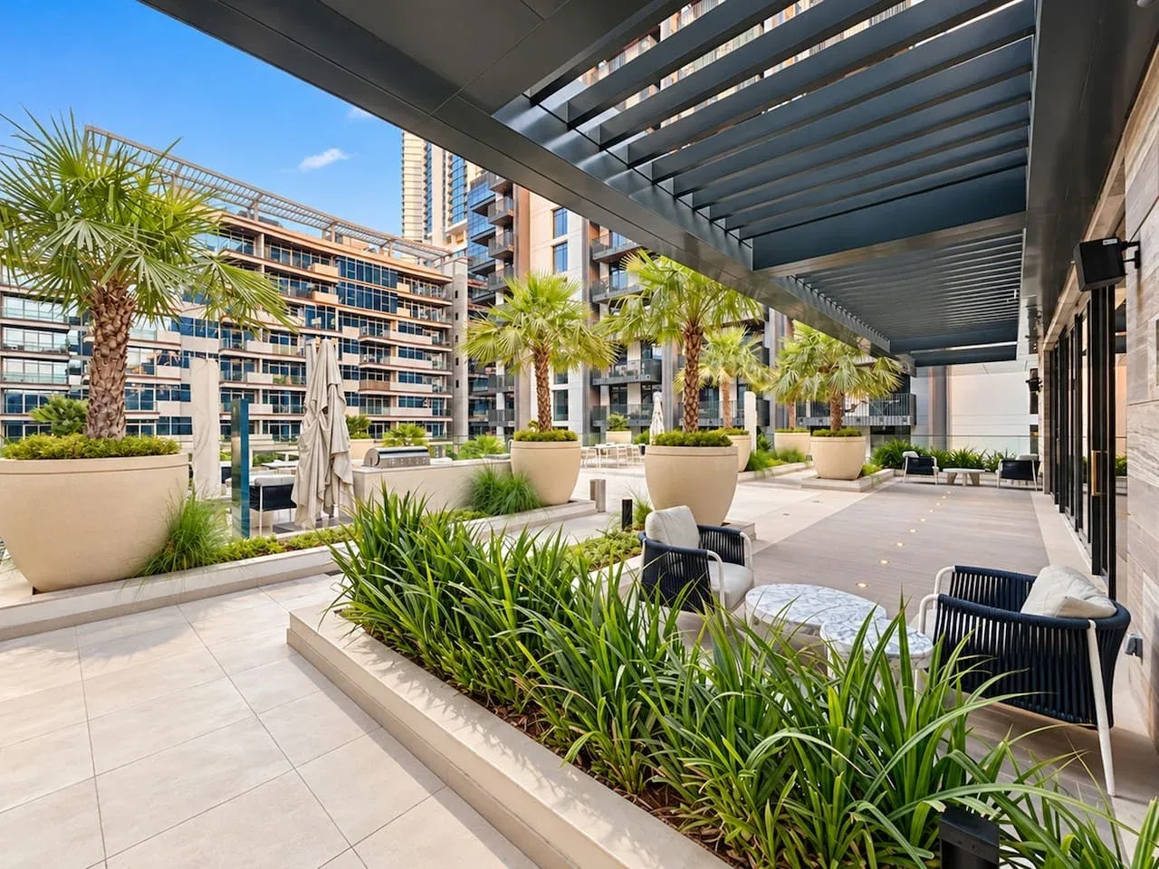 A landscaped outdoor terrace with seating, palm trees, and a slatted canopy.