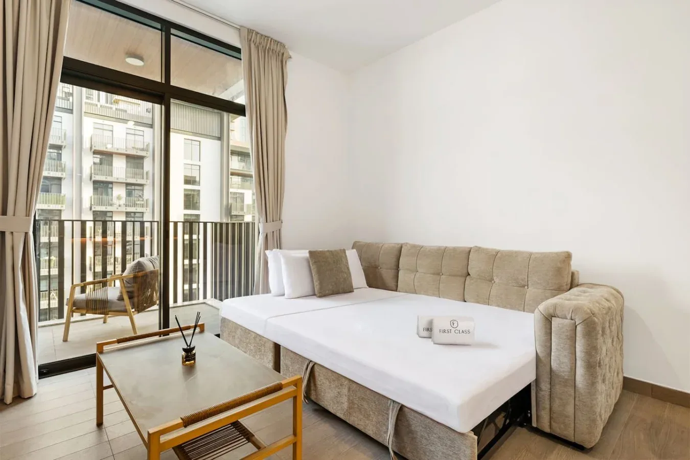 A living room with a sectional sofa, coffee table, and tall windows opening onto a balcony.