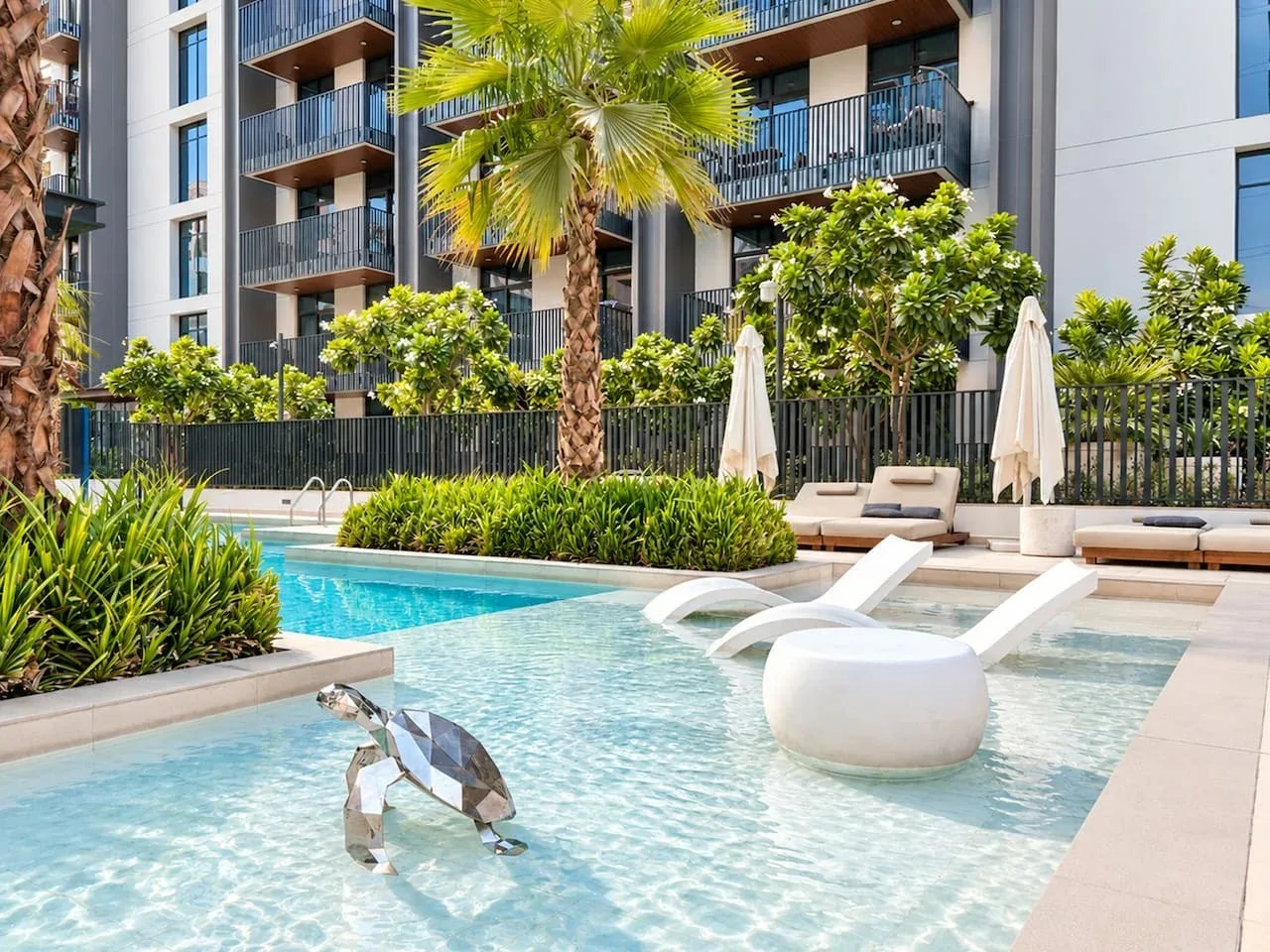 A modern outdoor pool sits beside a landscaped terrace and apartment building.