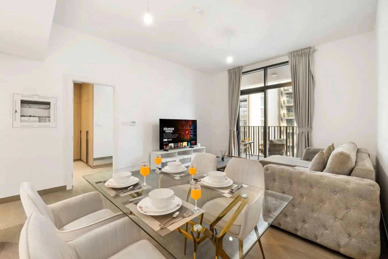 A bright living and dining area with seating, a glass table, and a television.