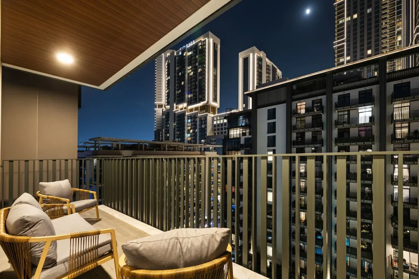 A furnished balcony at night overlooks illuminated high-rise buildings.