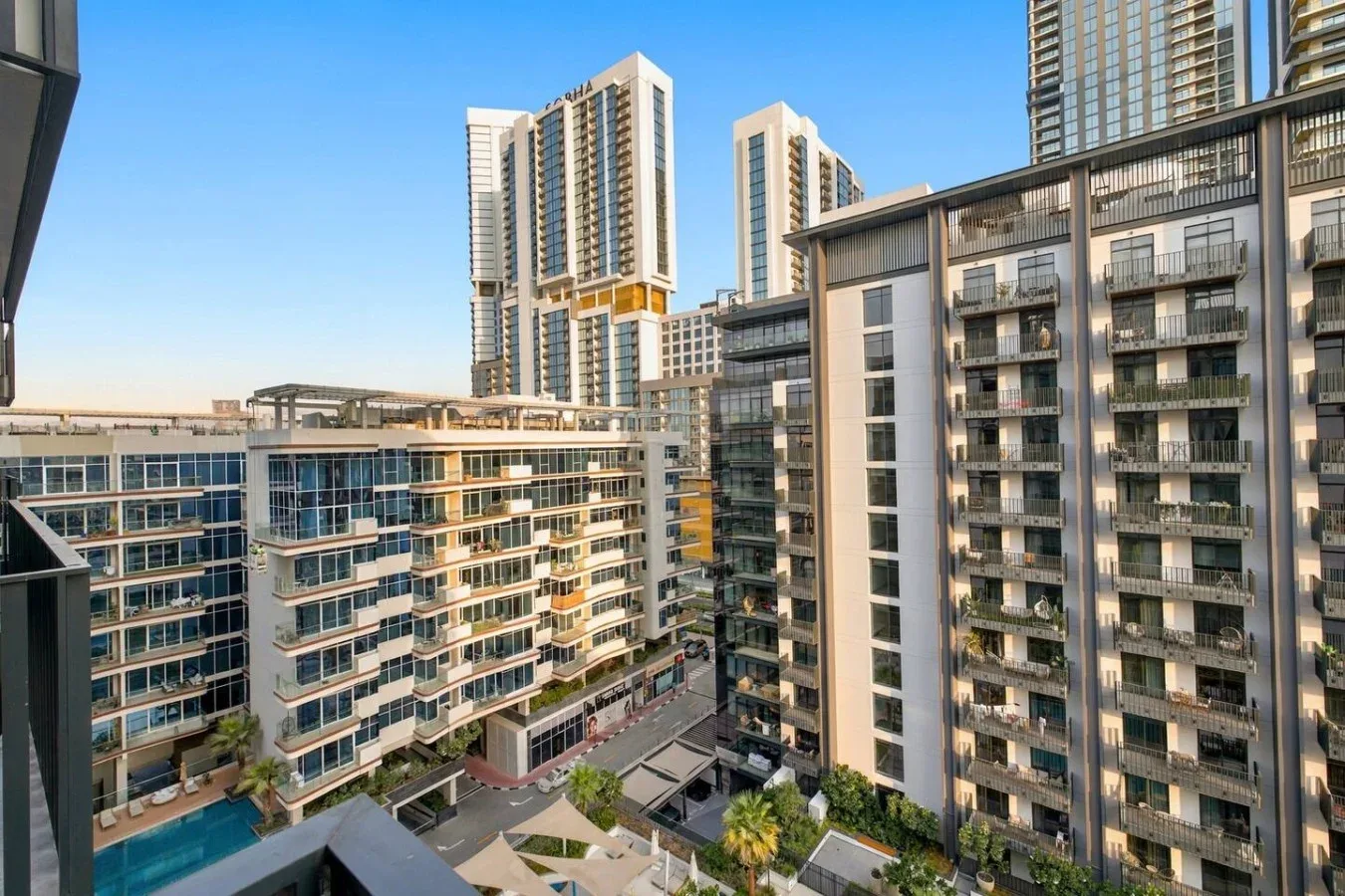 Modern high-rise buildings surround a courtyard with walkways and greenery.