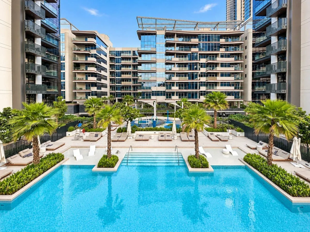 A courtyard pool sits among modern apartment buildings and palm trees.