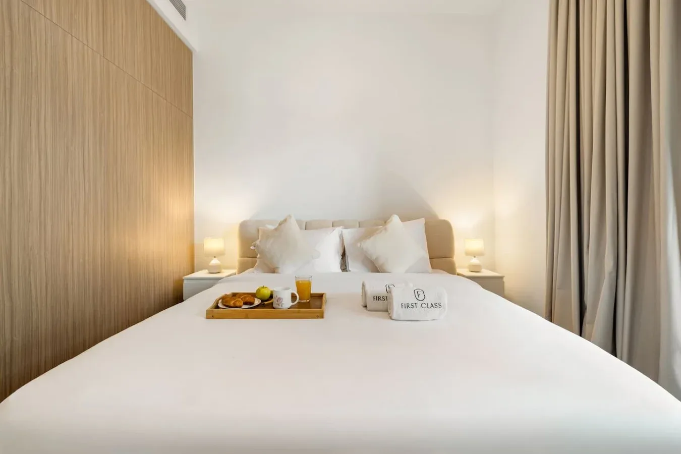 A neatly made bed with white linens, bedside lamps, and curtains.