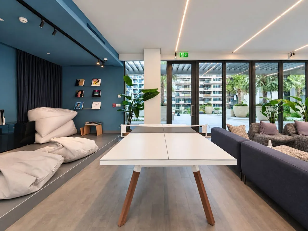A bright lounge with a table in the foreground and seating beside large windows.