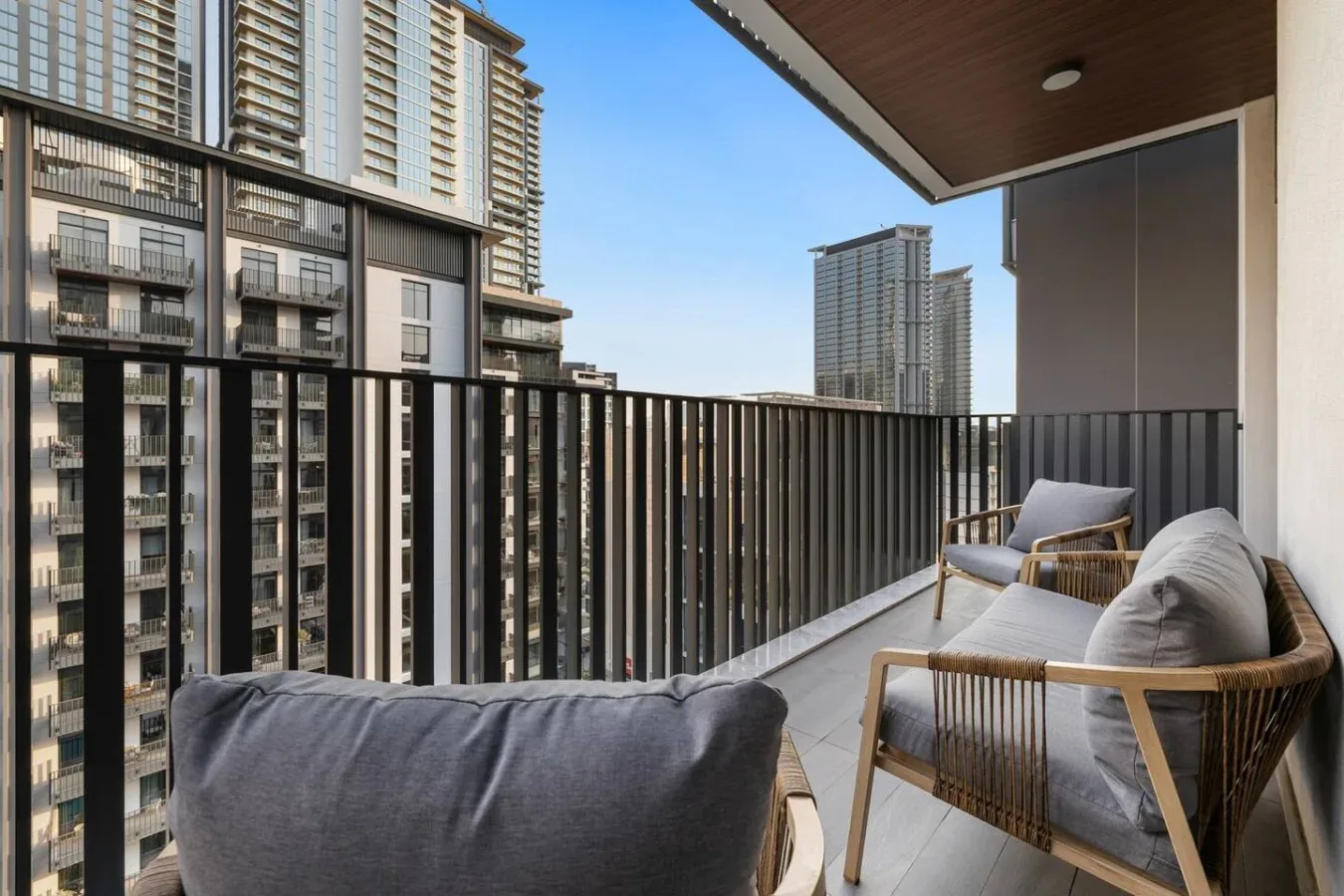 A balcony with cushioned seating overlooks nearby high-rise buildings.
