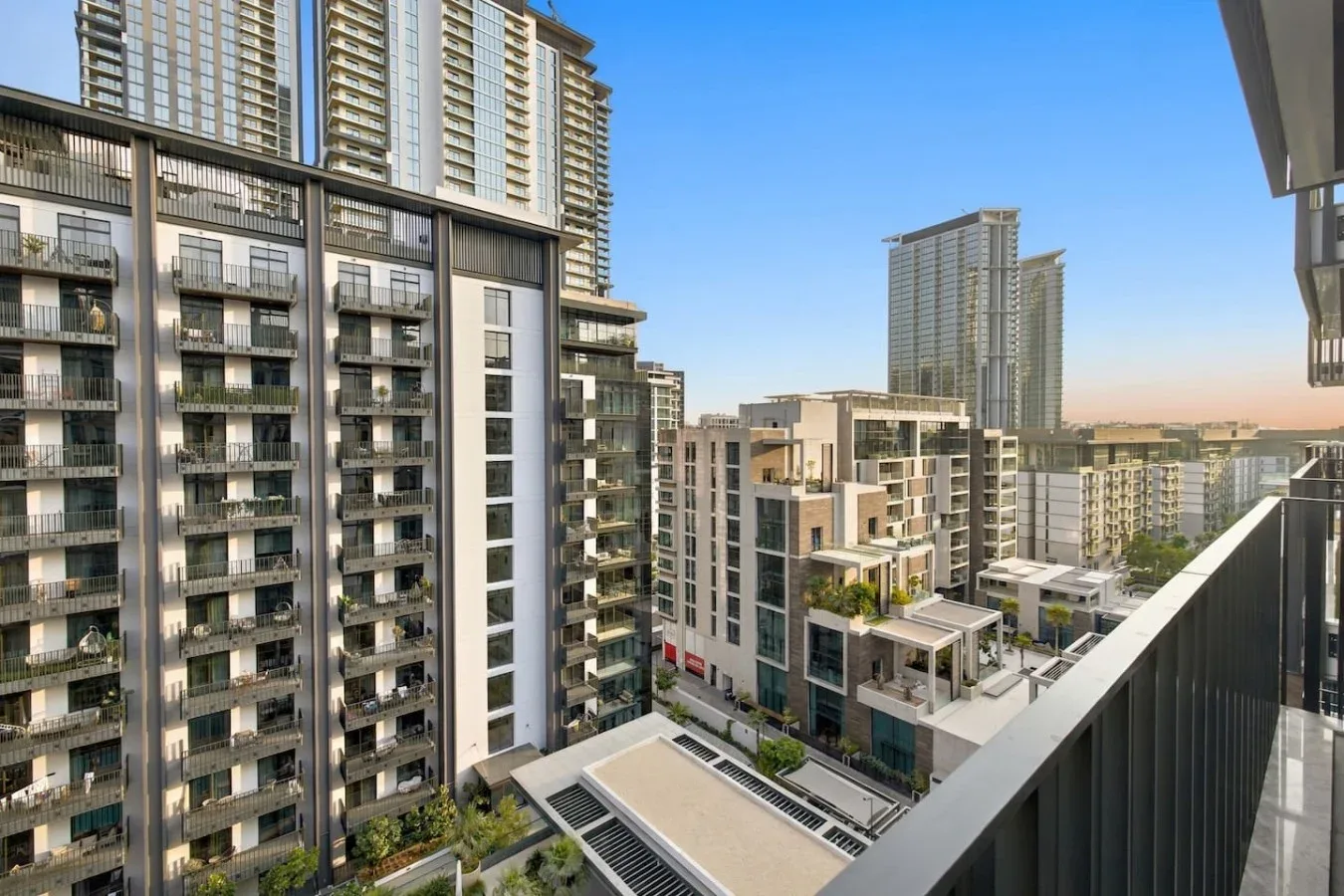 High-rise residential buildings fill the view from a balcony beneath a clear sky.