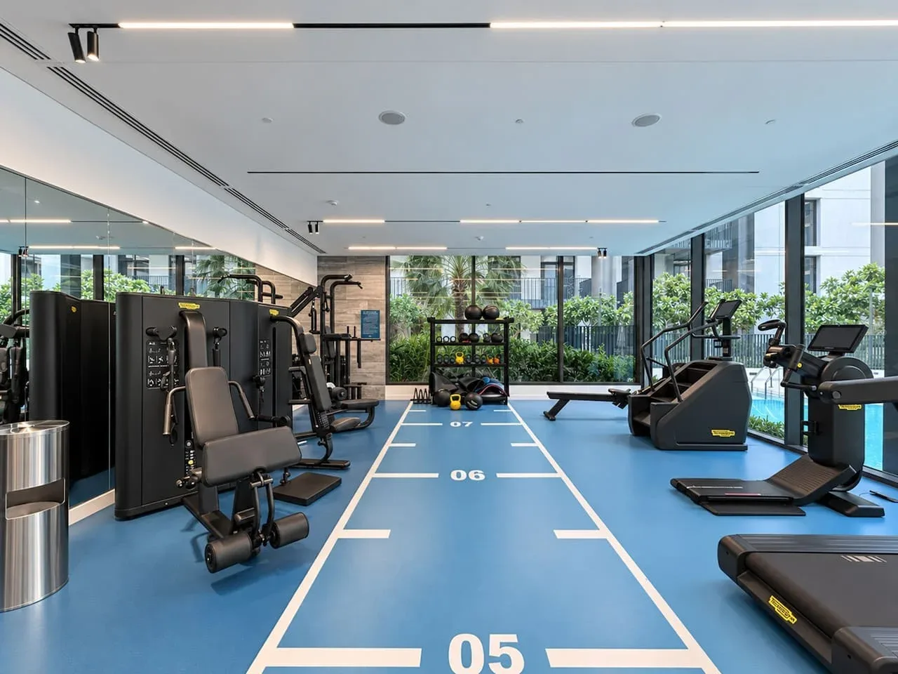 A bright gym with exercise machines and a marked blue floor.