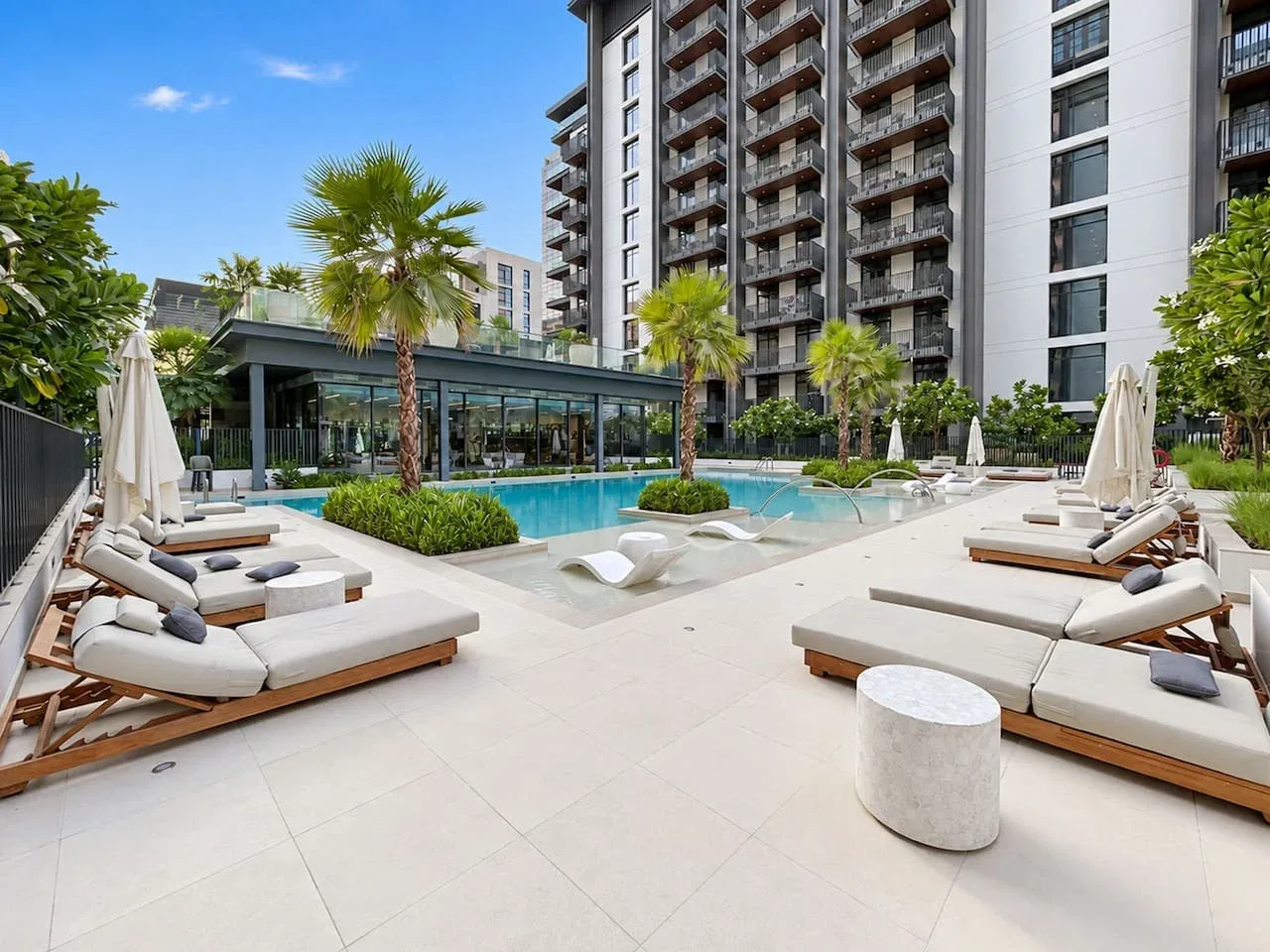 An outdoor swimming pool with lounge seating beside a modern high-rise building.