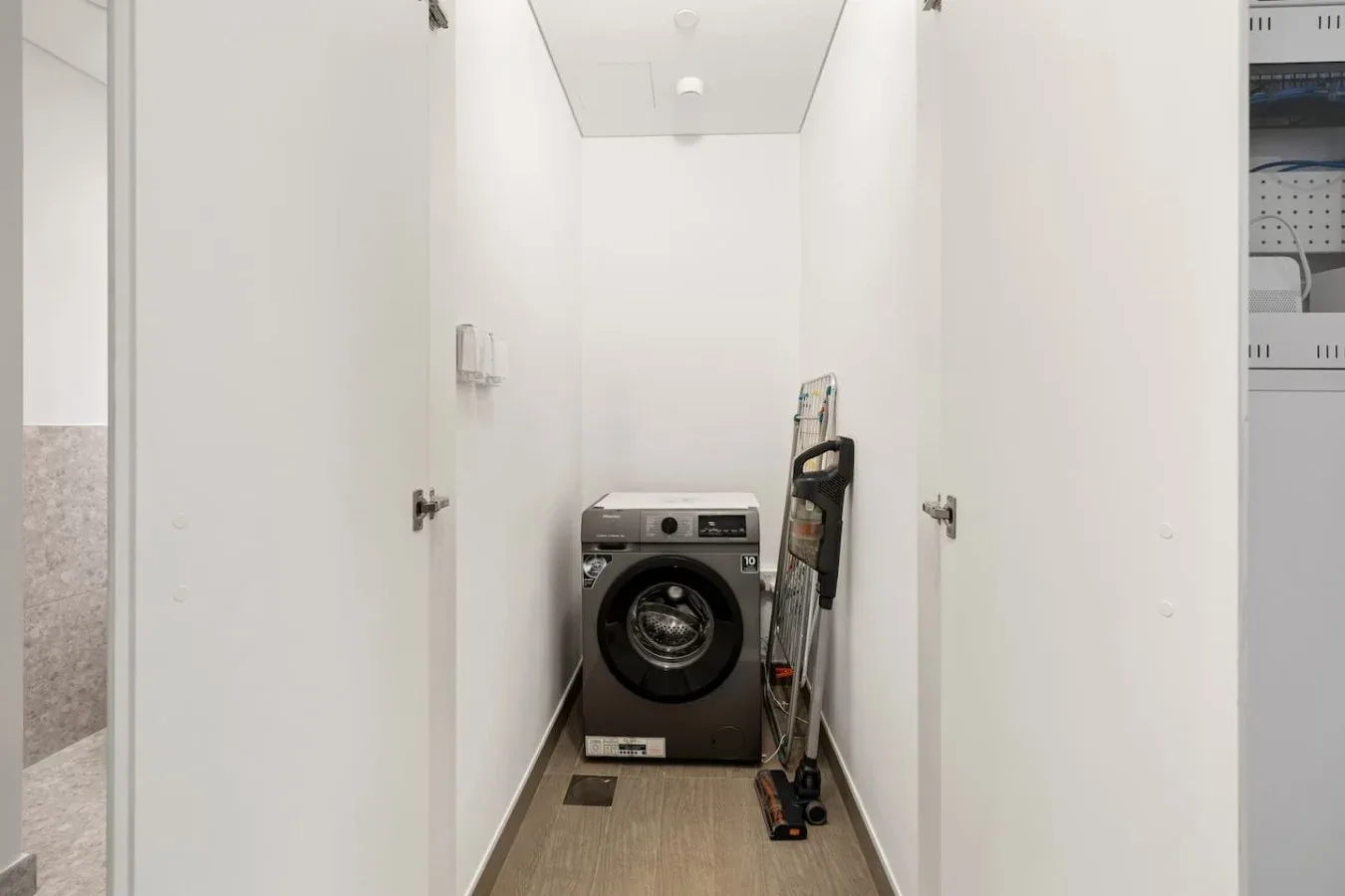 A narrow laundry room with a front-loading washing machine and cleaning equipment.