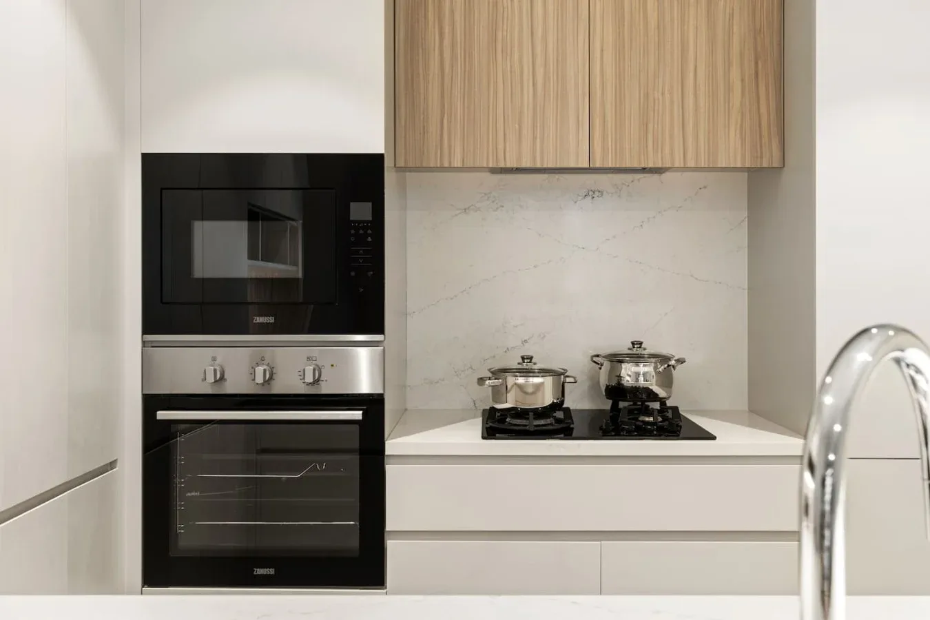 A modern kitchen with a cooktop, built-in oven, and light wood cabinets.