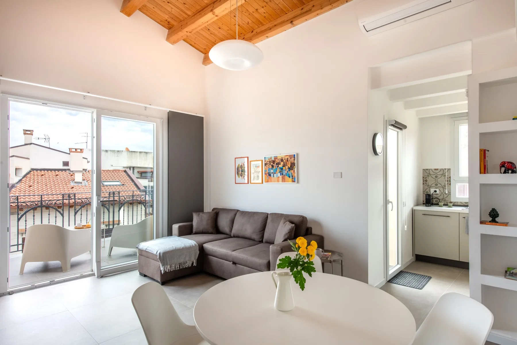 A bright living room with seating beside large windows and an open kitchen.