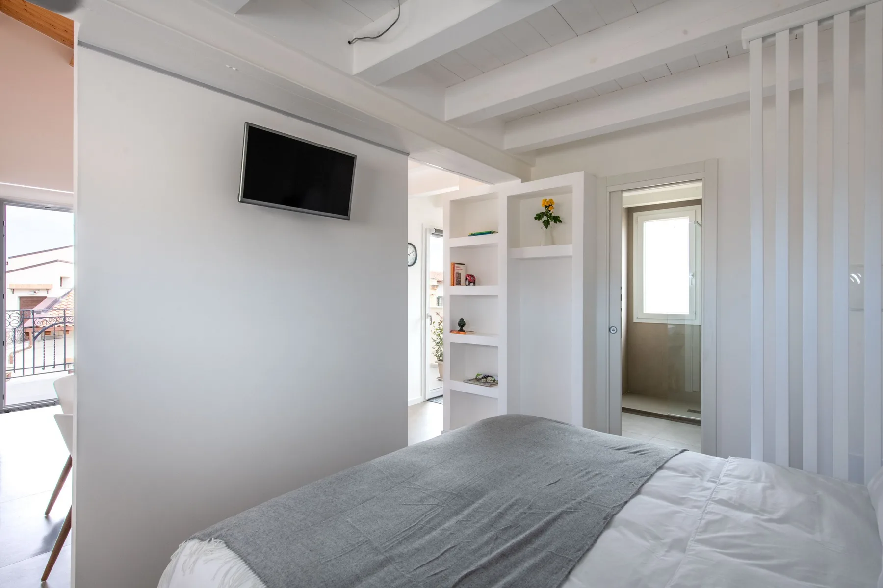A bright bedroom with a bed, wall-mounted television, and built-in shelving.