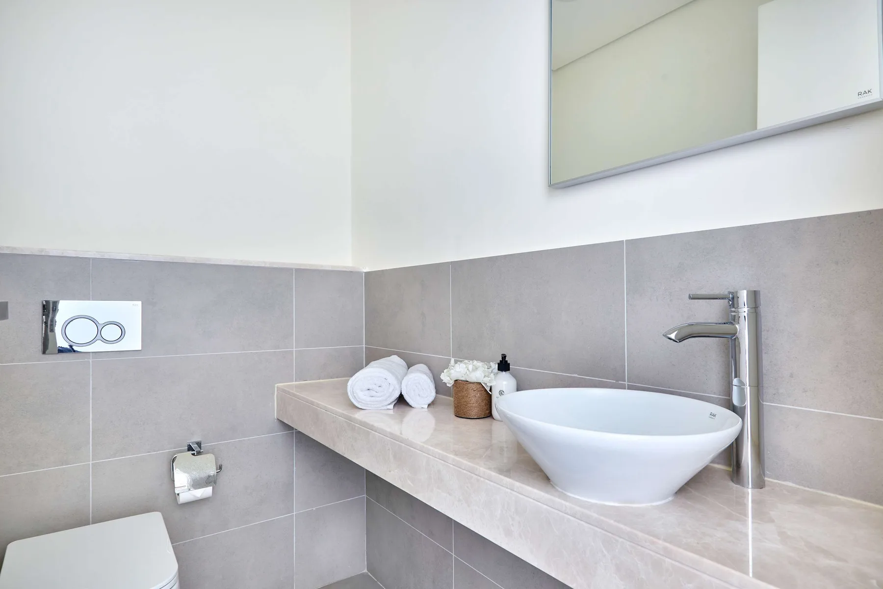 Un tocador de baño con lavabo blanco sobre encimera, grifo y paredes de azulejos grises.