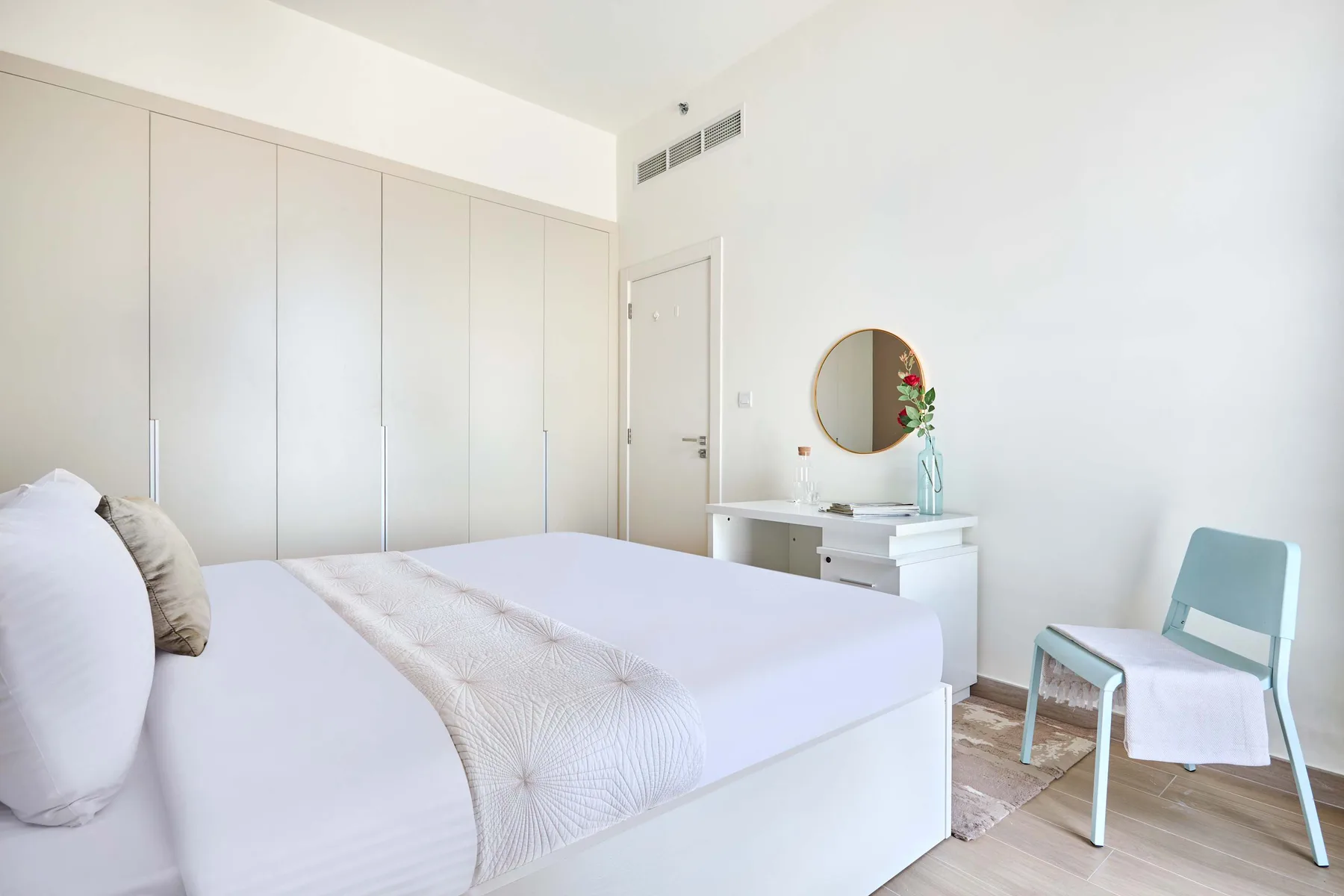 Un dormitorio luminoso con una cama tendida y un pequeño tocador.