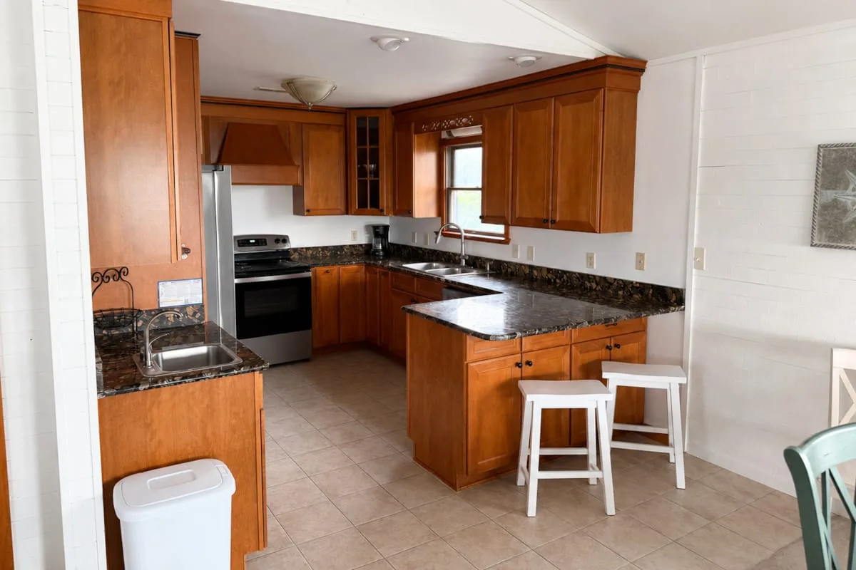Una cocina con gabinetes de madera, encimeras oscuras y asientos junto a la isla.