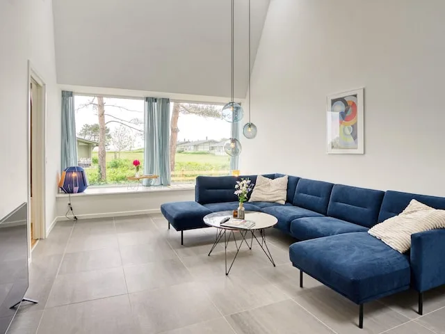 Una sala de estar luminosa con asientos azules y grandes ventanas con vistas a un jardín.