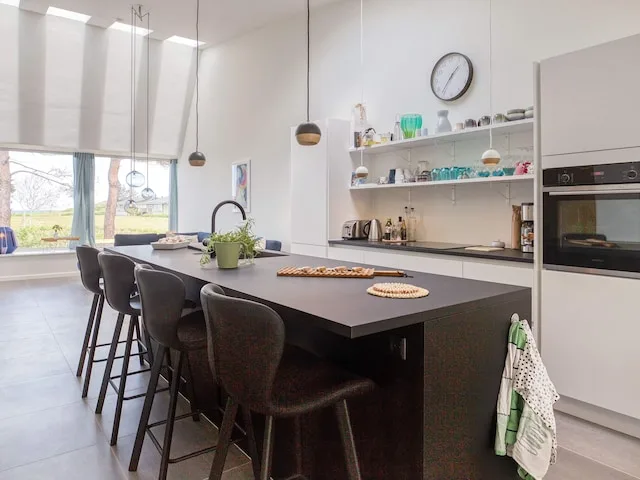 Una cocina moderna tiene una isla oscura con asientos y estantes abiertos.