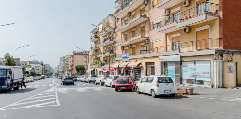 A city street lined with apartment buildings, shops, and parked cars.