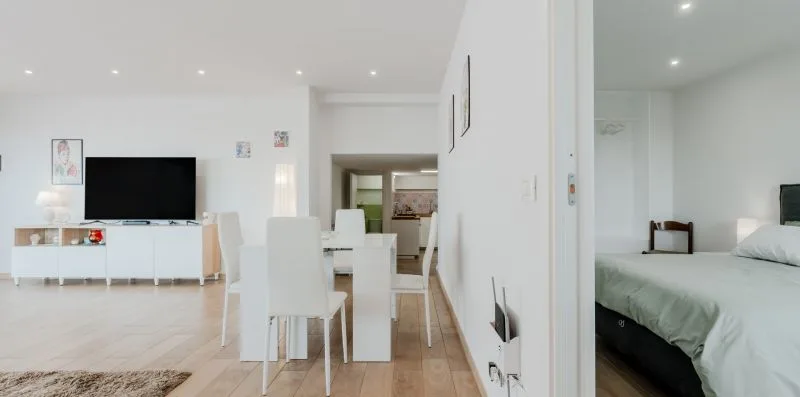 A bright dining area with a table and white seating beside a bedroom.