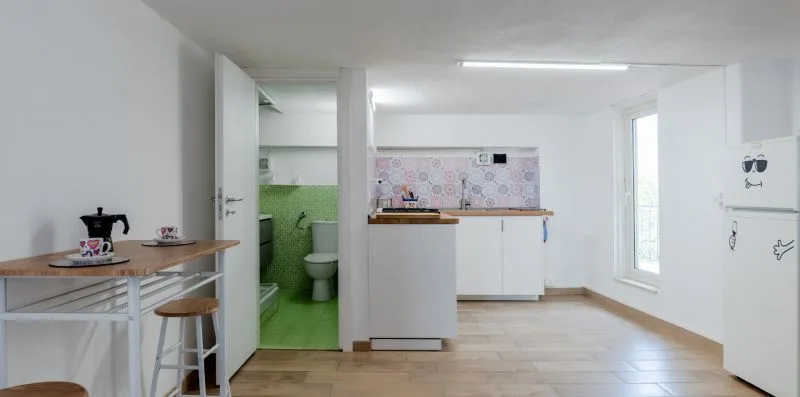 A bright kitchenette with a small dining table and an open bathroom doorway.