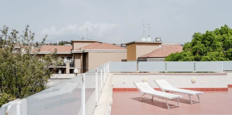 A rooftop terrace with sun loungers and a glass railing.