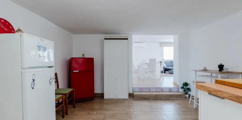 A kitchen with a white refrigerator and red refrigerator beside a dining area.