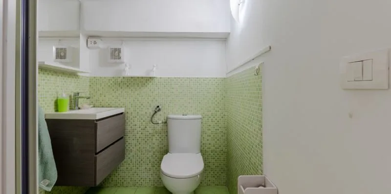 A small bathroom with a toilet, vanity, and pale green tiled walls.