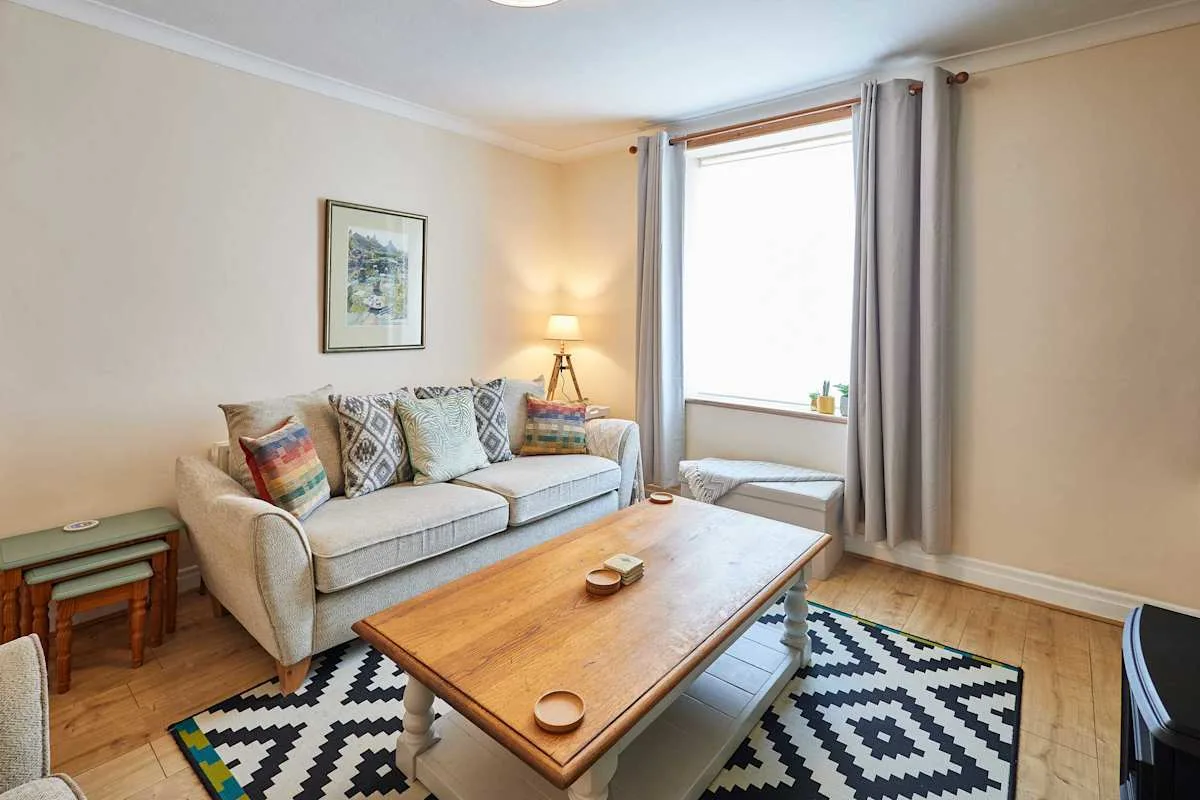 A bright living room with a sofa, wooden coffee table, and patterned rug.