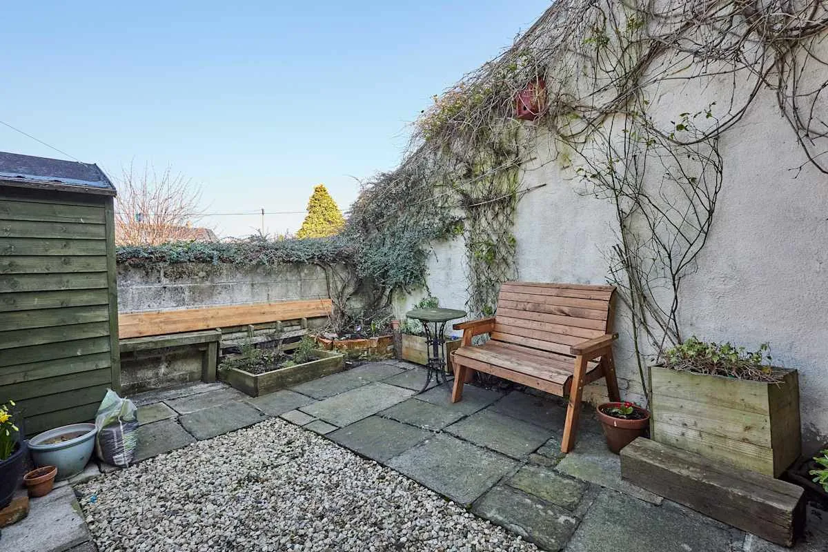 A paved courtyard with wooden benches, raised planters, and climbing vines.