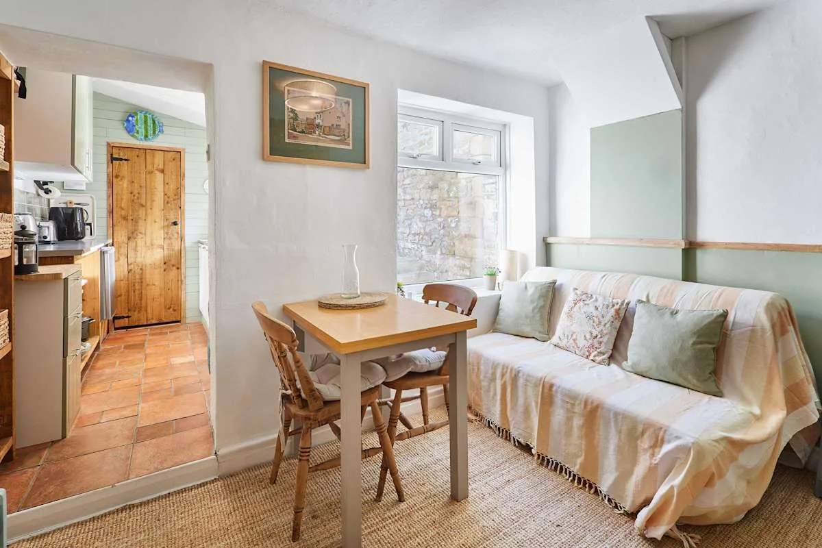 A bright sitting area with a dining table beside a sofa and adjoining kitchen.