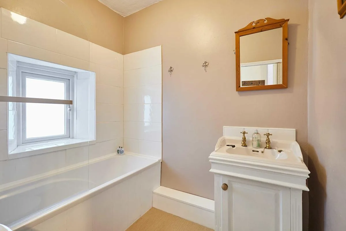 A bathroom with a bathtub, window, and pedestal sink.