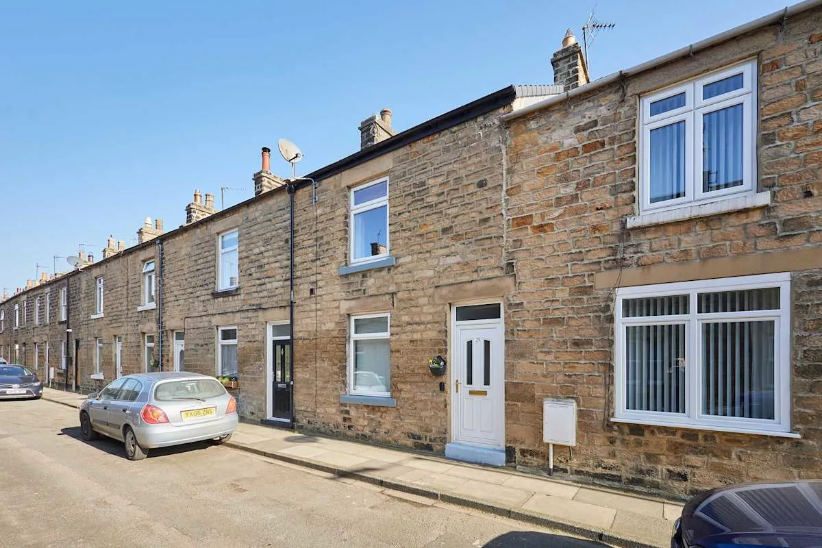 A row of stone-fronted houses lines a residential street with parked cars.