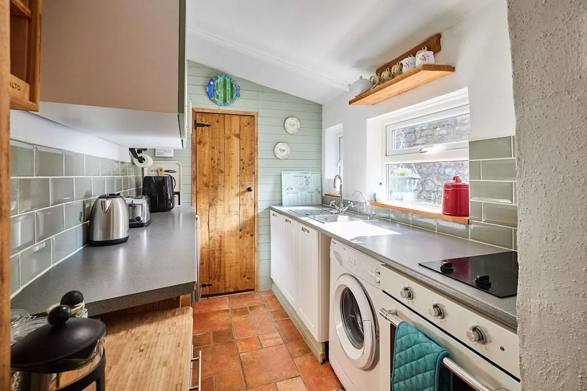A compact kitchen with a wooden door, countertop appliances, and a washing machine.