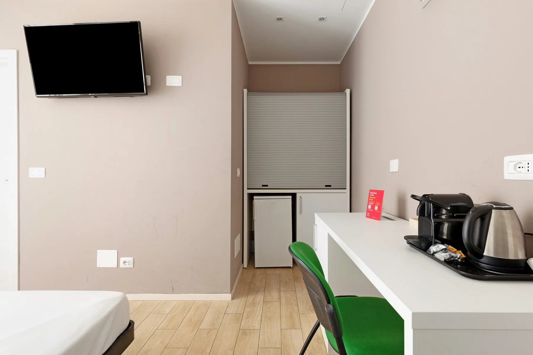 A compact room with a bed, wall-mounted television, and counter seating.