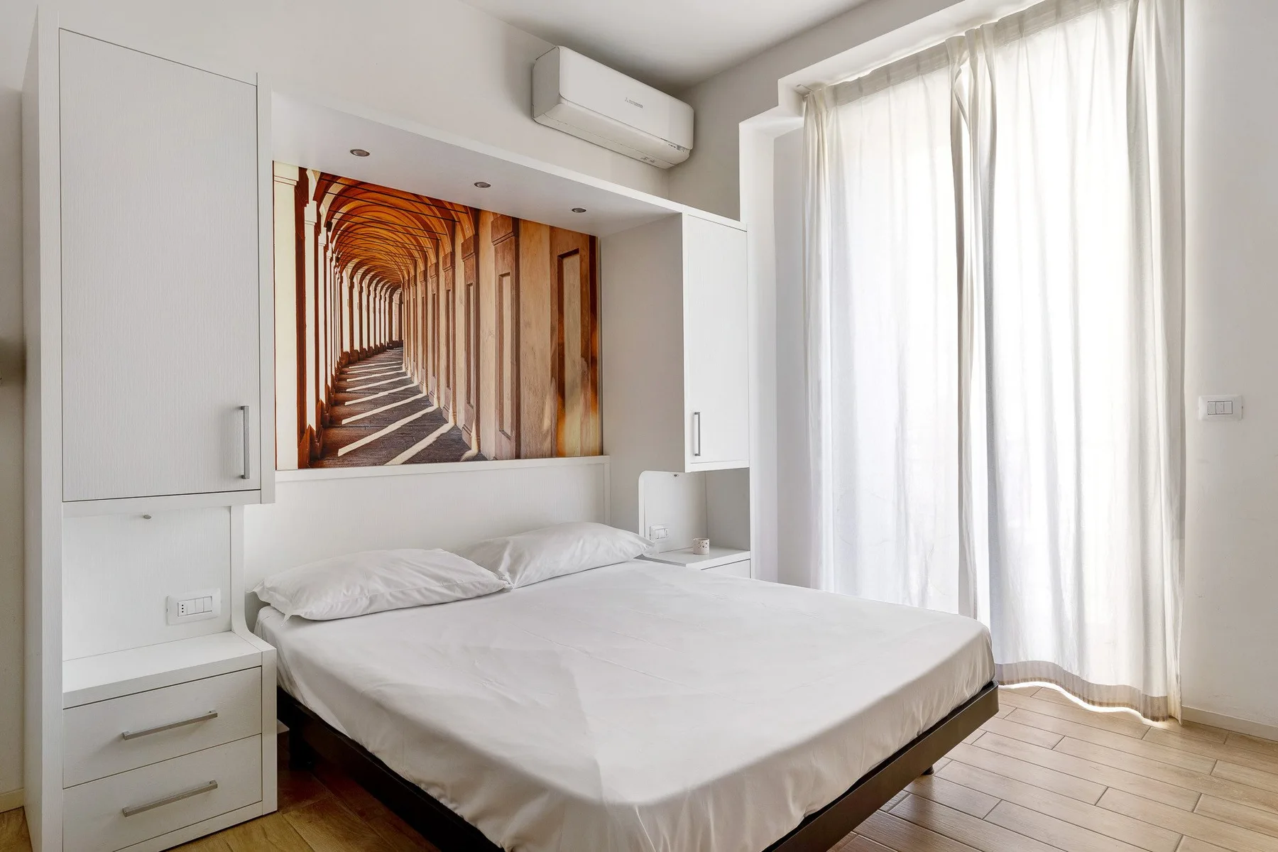 A bright bedroom with a bed beneath a framed architectural photograph.