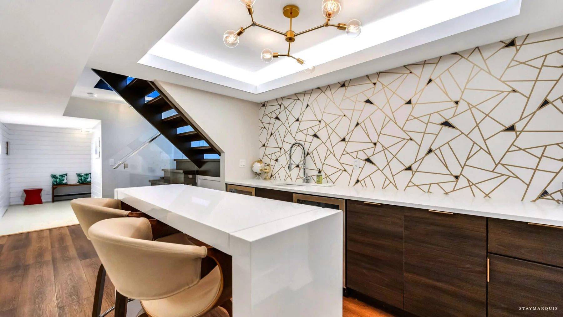 A modern kitchen with a long white island, seating, and geometric wall artwork.