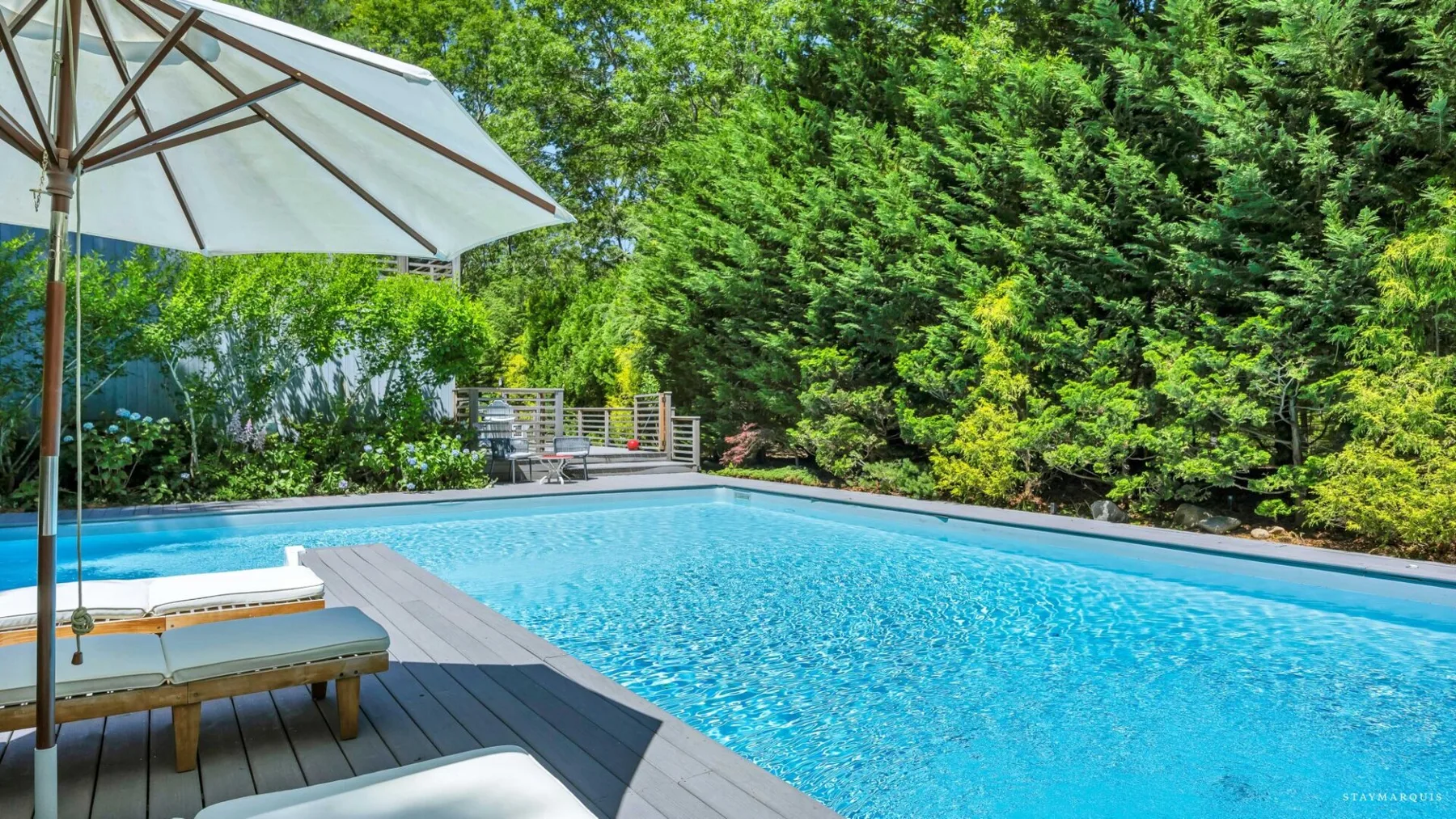 An outdoor swimming pool sits beside a wooden deck and dense greenery.