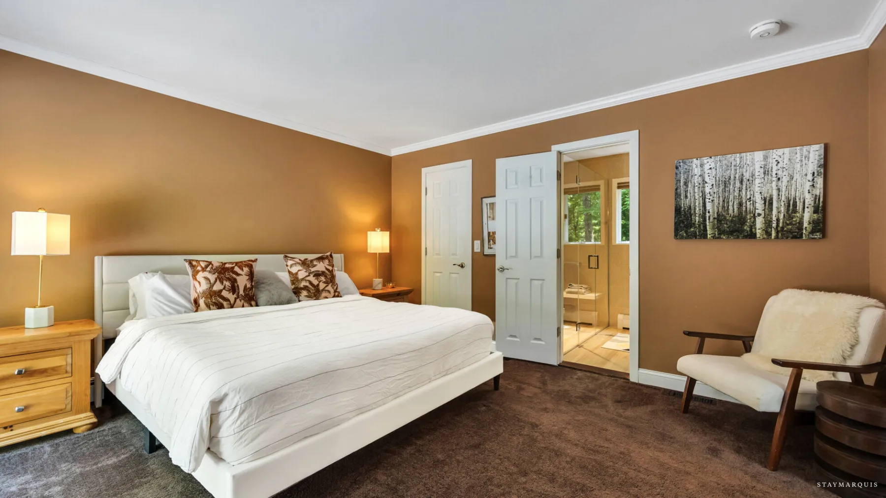A bedroom with a white bed, bedside tables, and an open doorway.