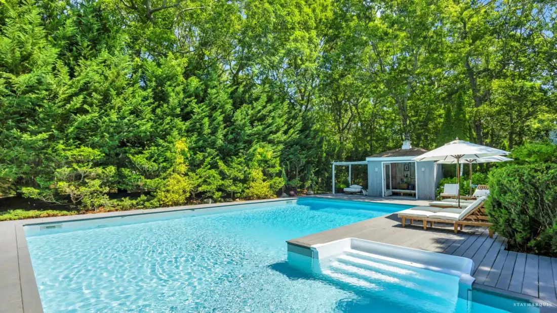 A swimming pool with steps sits beside a wooded garden.