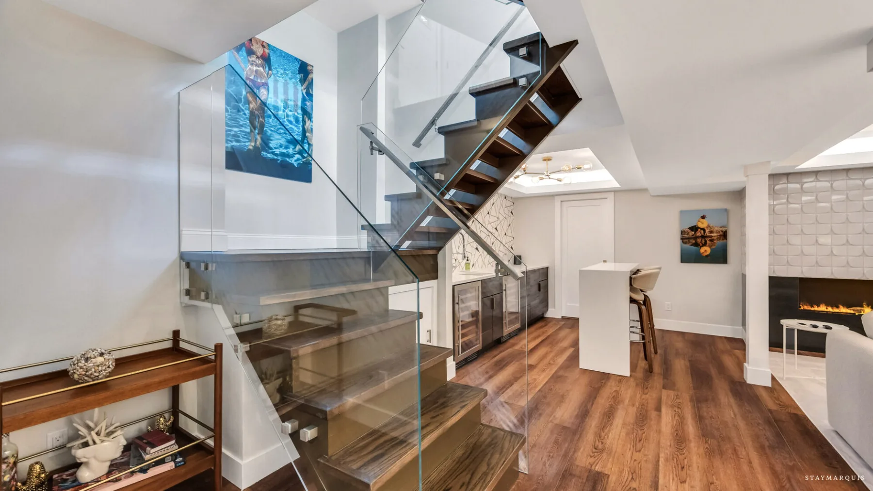 A bright open-plan interior with a wood staircase, glass railing, and kitchen island.