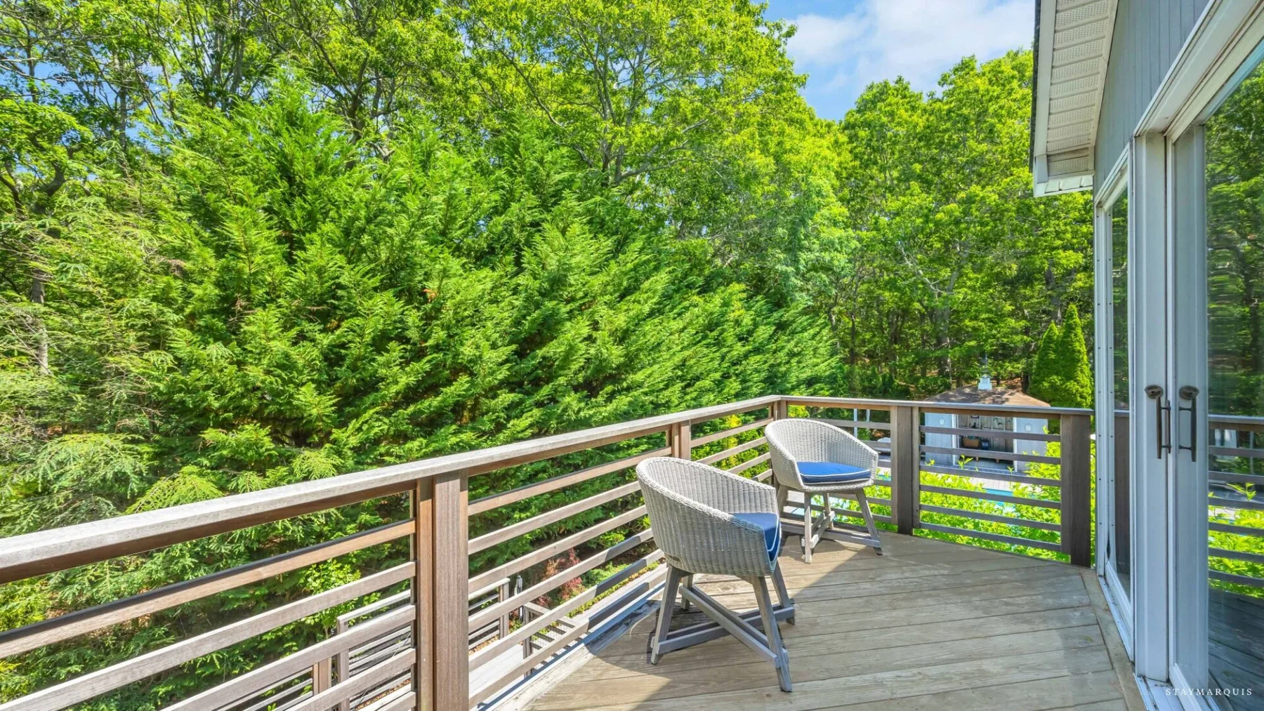 A wooden deck with outdoor seating overlooks a lush green tree canopy.