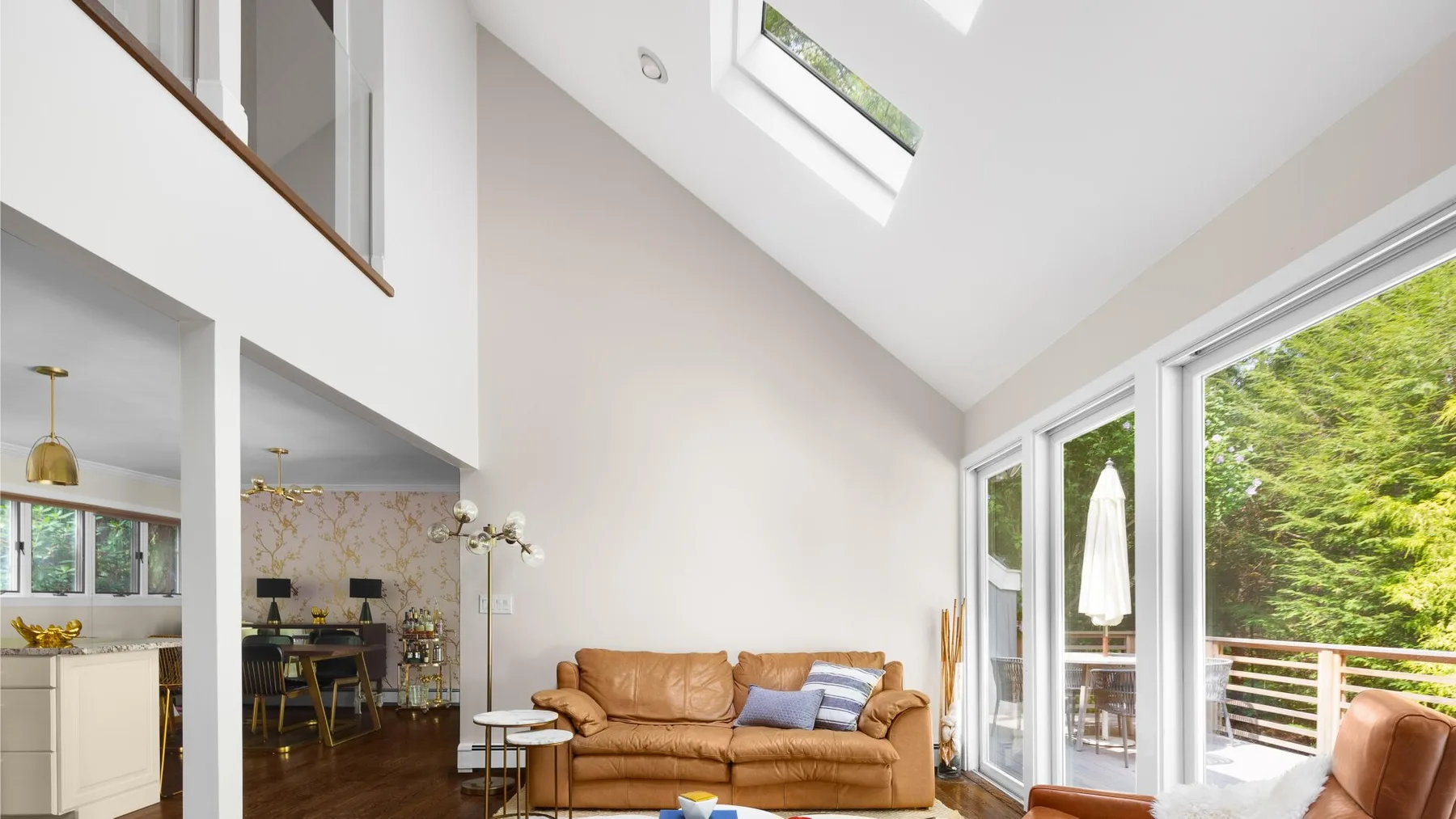 A bright living room with a brown sofa beside large glass doors opening to a deck.