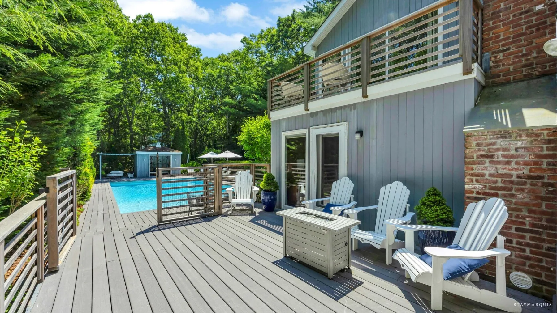 An outdoor deck with seating overlooks a swimming pool and surrounding trees.