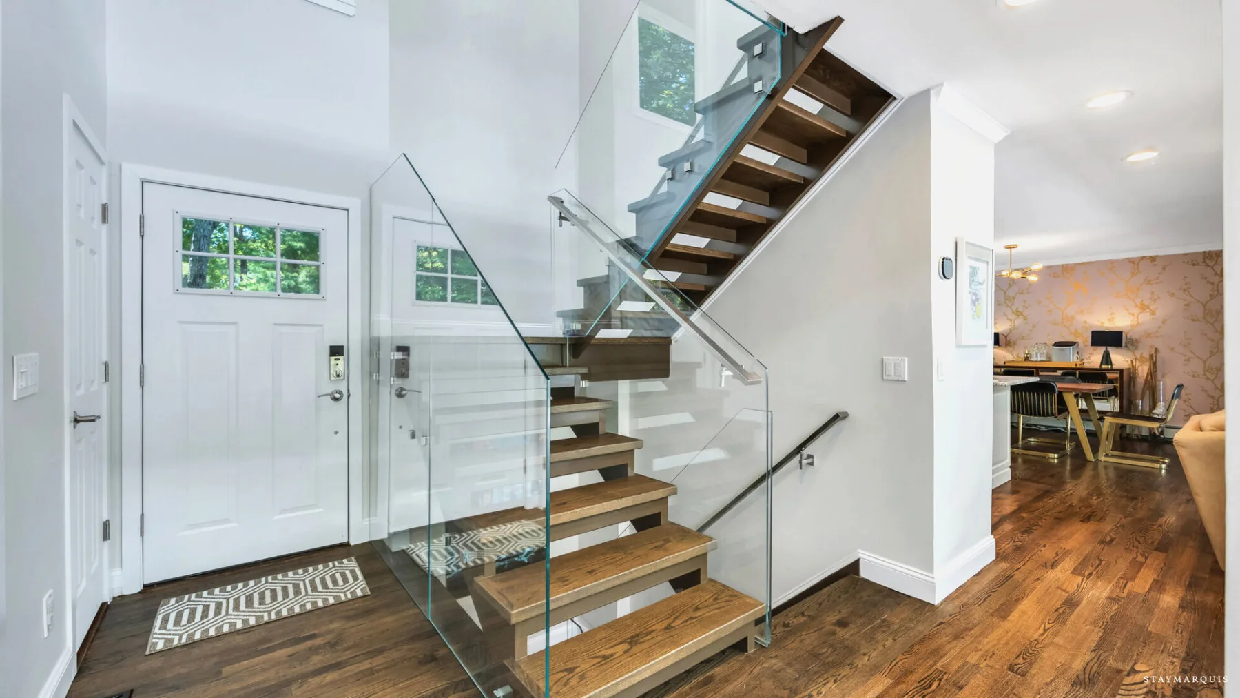 A bright entryway with a white front door and an open staircase beside the living area.
