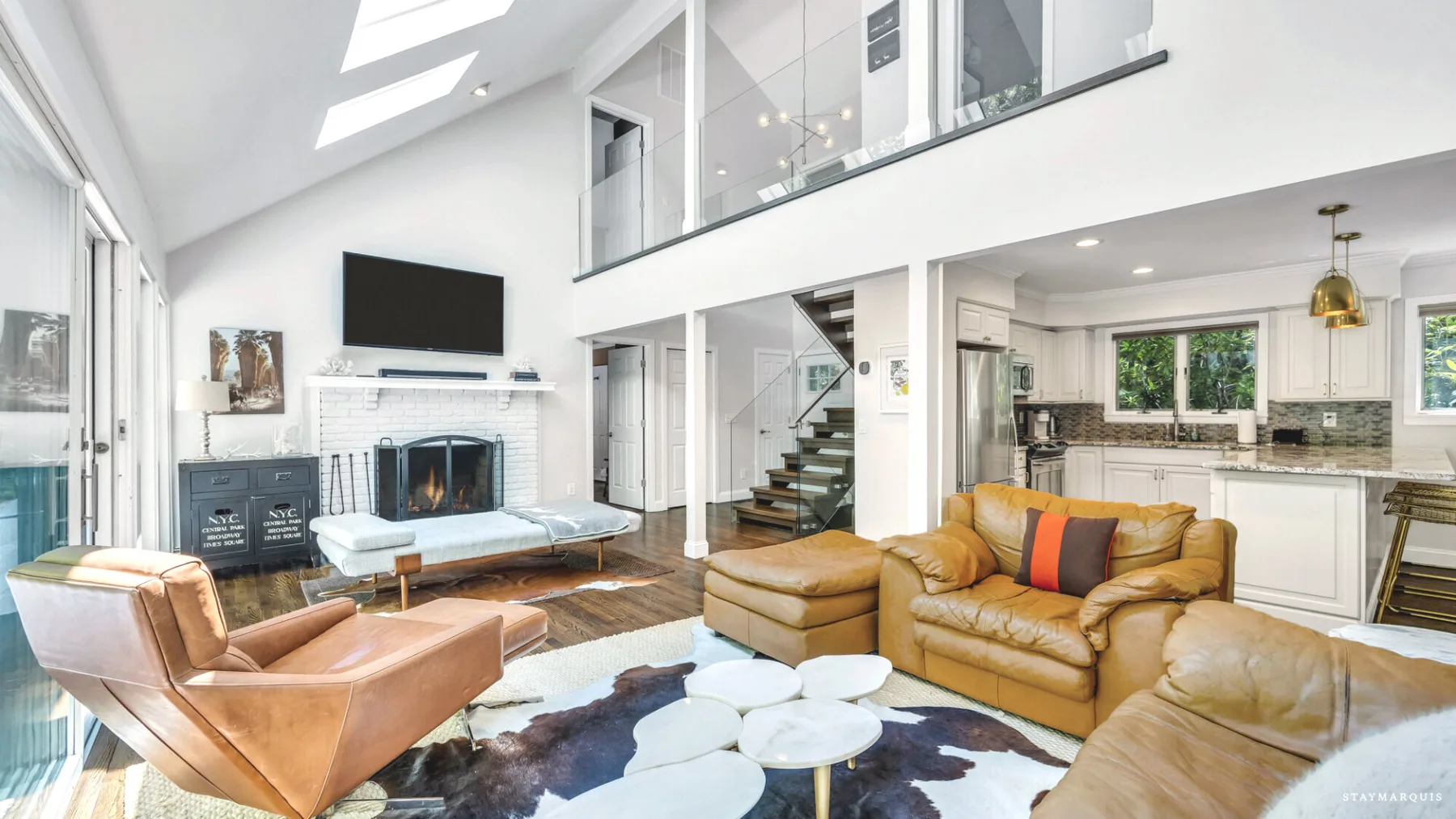 A bright open-plan living room with seating, a fireplace, and an adjoining kitchen.