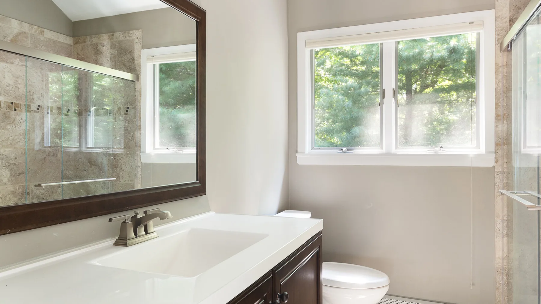 A bathroom with a wide vanity, mirror, toilet, and window.