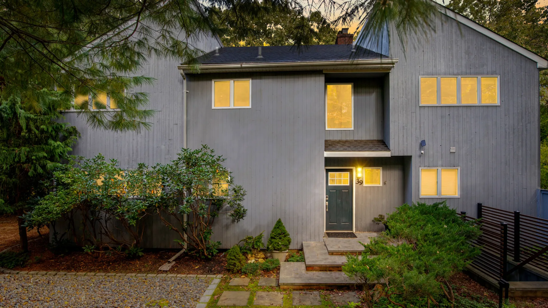 A gray house exterior with lit windows and a stone walkway.